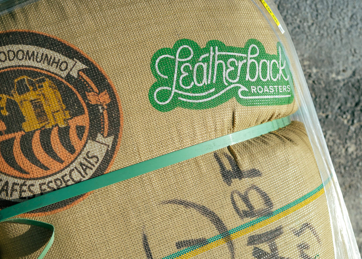 A close-up of a burlap sack with printed branding, including a green 'Leatherback Roasters' logo wrapped in a clear plastic sleeve.