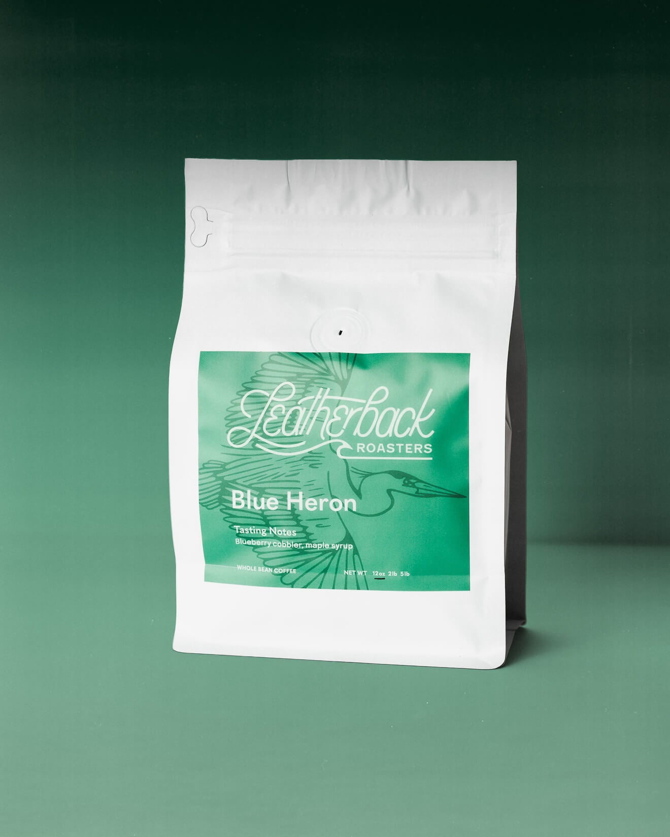 A white valved coffee bag with a green front label reading 'Leatherback Roasters' and 'Blue Heron', photographed on a green gradient background.
