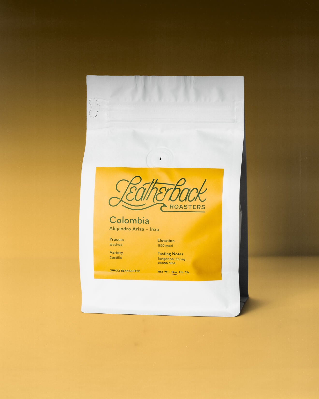 A white valved coffee bag with a large orange front label reading Leatherback Roasters Colombia, photographed against a warm brown-to-yellow gradient background.