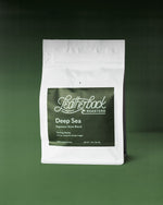 A 12oz white valved coffee bag with a large Dark Green label reading Leatherback Roasters and Deep Sea Espresso, photographed against a soft green gradient background.
