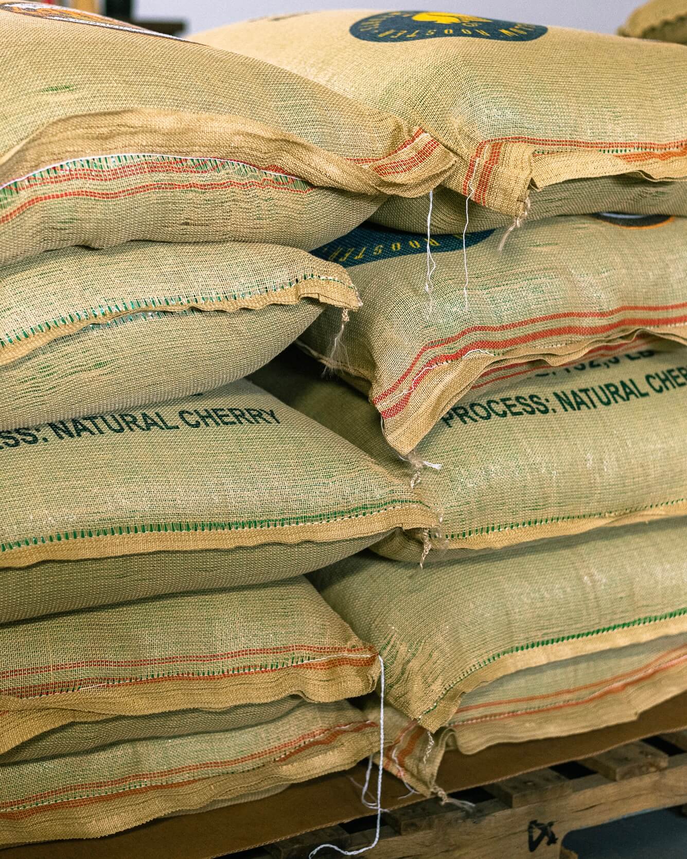 Stack of burlap bags with 'Process Natural Cherry' text on a wooden pallet.