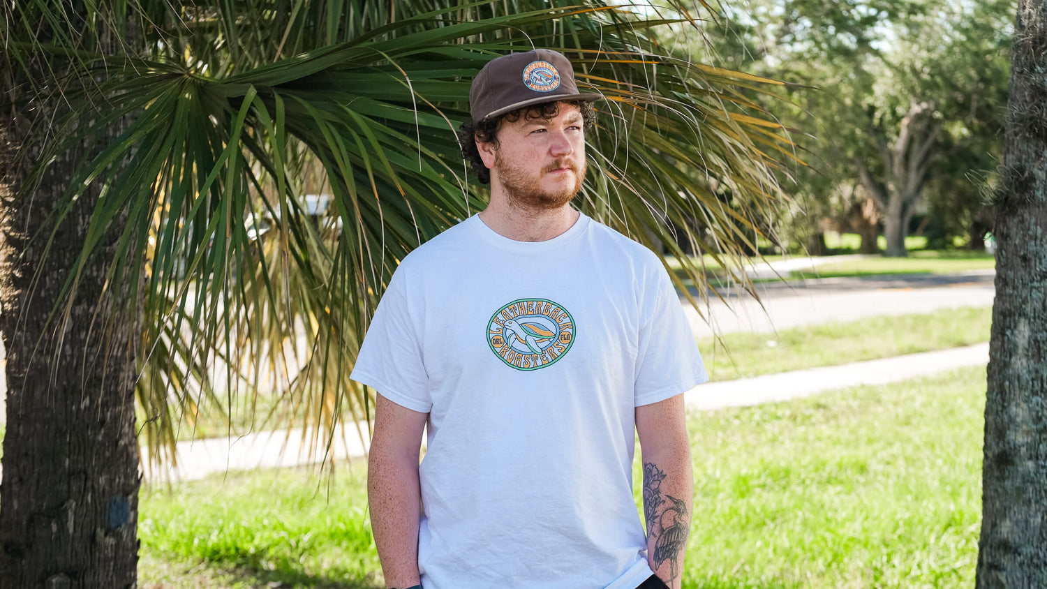Man standing outside wearing a white tee shirt and a brown hat with Leatherback Roasters turtle logo.