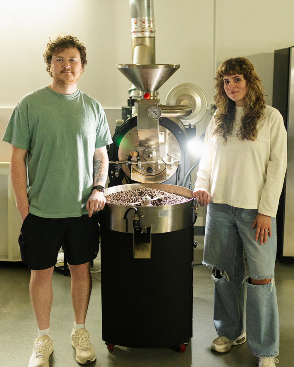 Two people standing next to a coffee roasting machine in a modern specialty coffee roastery.
