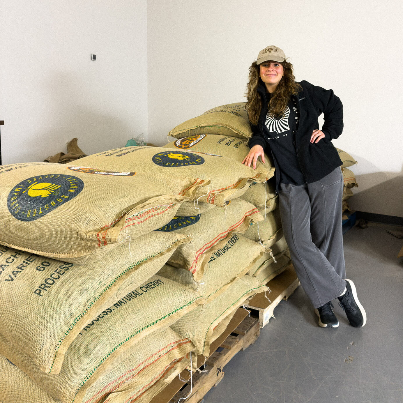 Person leaning against a stack of large Brazilian coffee bags in Leatherback roastery