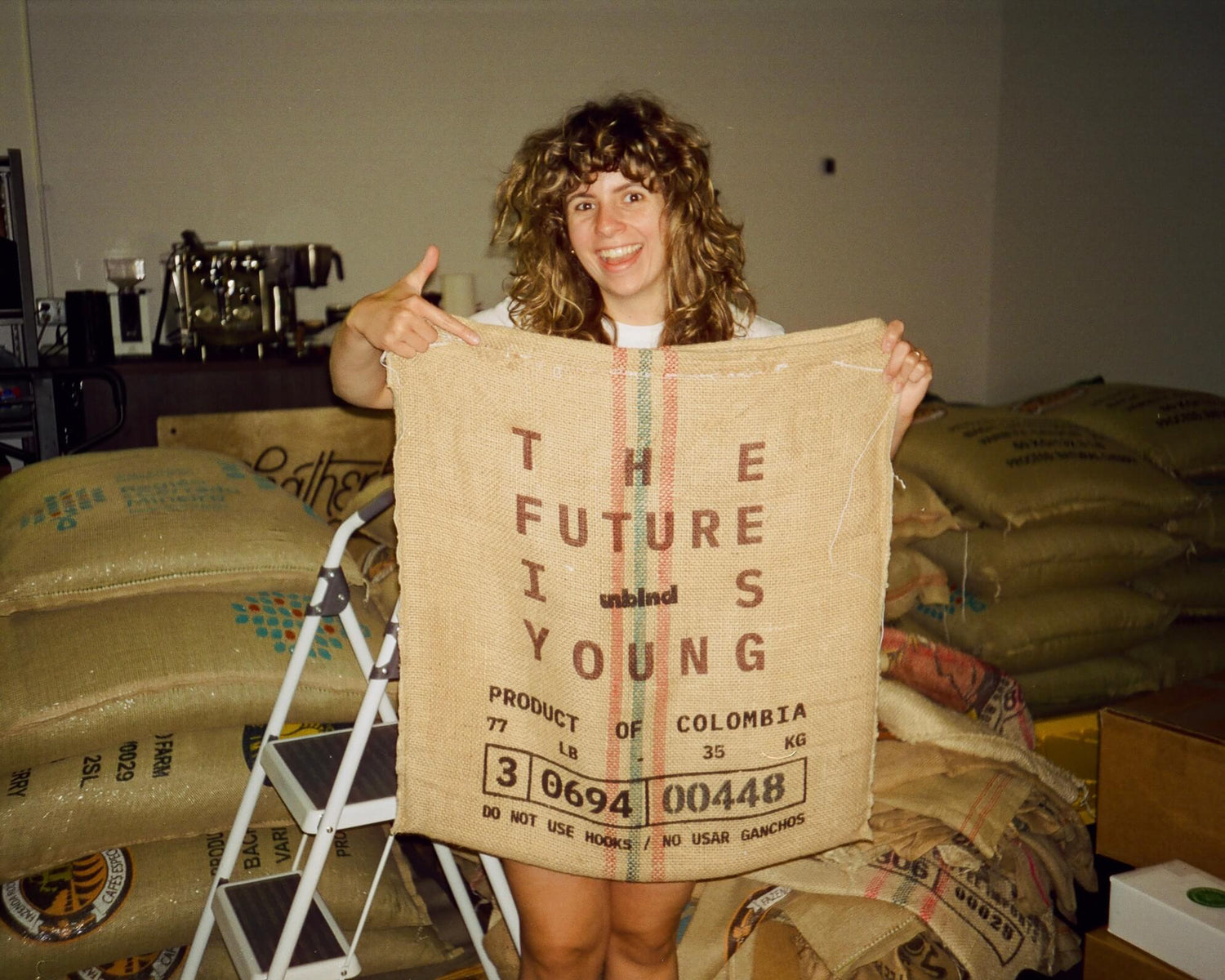 Woman holding a large burlap coffee sack with text in a Coffee Roastery.